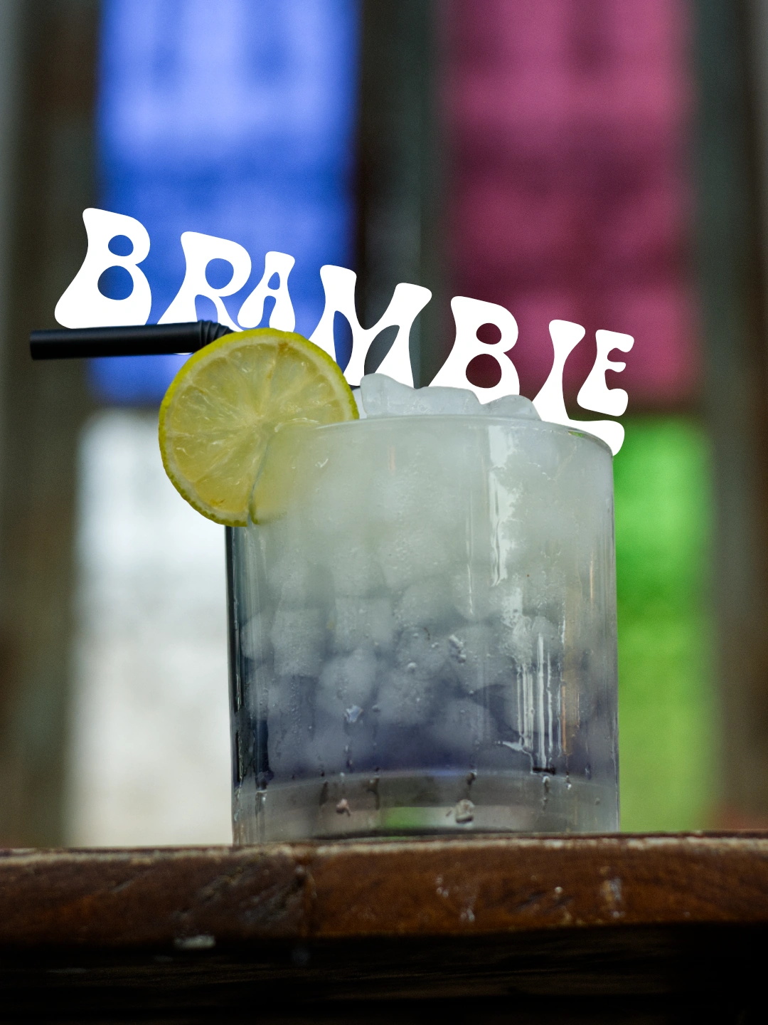 Cóctel Bramble de Zaraho con hielo y lima, ante los cristales de colores de la barra.